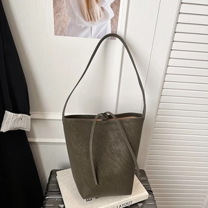Detail of olive green matte leather bucket bag with drawstring knot on travel suitcase