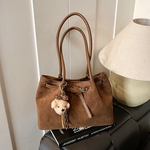 Detail of a large brown suede tote bag with metal buckle strap and plush bear charm