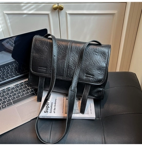 Detail of minimalist black crossbody bag with vintage texture on a leather sofa