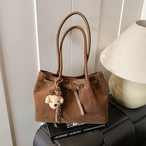 Close-up of dark brown suede tote bag with belt detail and plush puppy charm