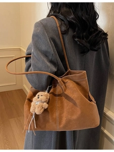Brown suede tote bag with white stitching and bear charm shown on model in a minimalist room