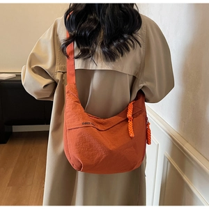Orange crescent canvas bag with THREE TREE logo shown on a model in a khaki trench coat