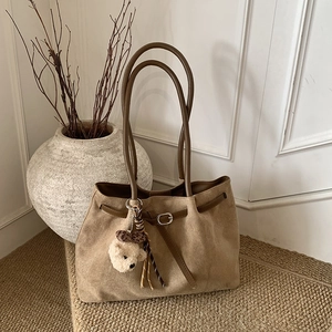 Close-up of a large khaki suede tote bag featuring a teddy bear charm on a woven carpet