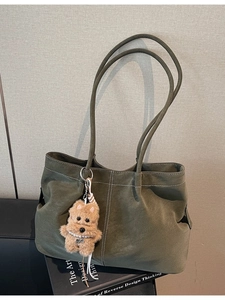 Olive green minimalist tote bag with contrast stitching and plush dog charm on a book