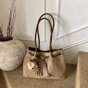 Close-up of khaki suede tote bag with leather strap detail and plush bear charm
