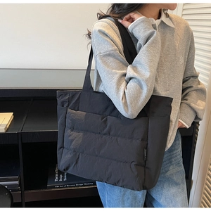 Detail view of the black quilted puffer tote bag with side logo tag and soft nylon texture