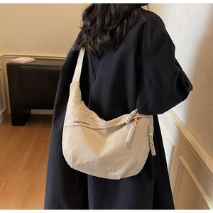 Close-up of beige canvas crescent bag with wide strap and braided rope zipper detail