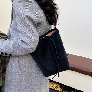 Minimalist black leather bucket bag worn with winter wool coat against autumn background