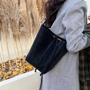 Close-up of black suede bucket bag showing soft texture and strap against autumn leaves