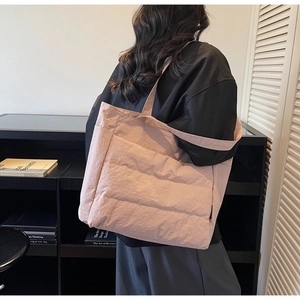 Detailed view of pink quilted puffer tote bag with wide strap on shoulder of a model