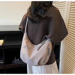 Close-up of a light grey crescent nylon crossbody bag worn by a model in casual style