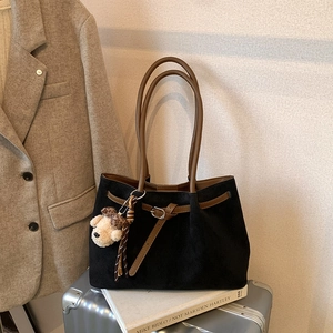 Close-up of black suede tote bag with brown leather handles and a cute plush bear charm