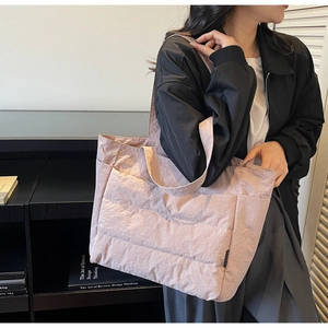 Detail of quilted large tote bag in light pink nylon with side pockets and smooth texture