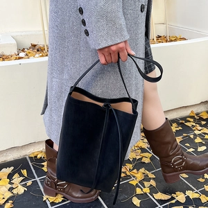 Detail of a black bucket bag in frosted texture carried by a model in autumn setting