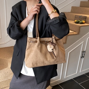 Brown frosted leather tote bag detail with white plush bear charm and buckle strap