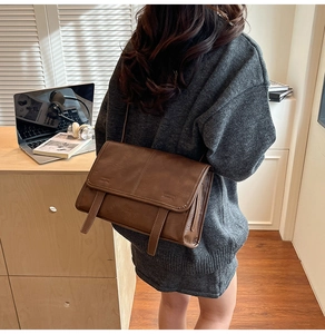 Detail view of a chocolate brown matte leather crossbody bag worn by a model in office