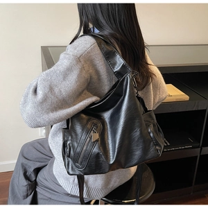 Close-up of black glossy leather tote bag featuring multiple pockets and wide shoulder straps