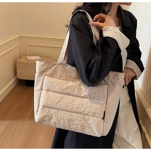 Detailed side view of a large beige quilted tote bag worn over the shoulder for daily commute