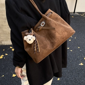 Detail of dark brown faux suede tote bag with plush bear charm on outdoor stone path