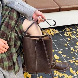 Detail of dark brown suede bucket bag with decorative drawstrings in an autumn setting