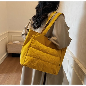 Model wearing a large yellow quilted puffer tote bag with a soft down-like texture