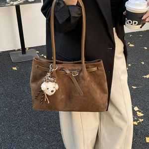 Detail of dark brown suede tote bag with plush dog charm against autumn ginkgo leaves
