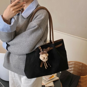 Detailed view of a large black suede tote bag with brown straps and a cute plush bear charm