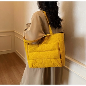 Detail of yellow quilted tote bag showing side pocket and padded nylon texture