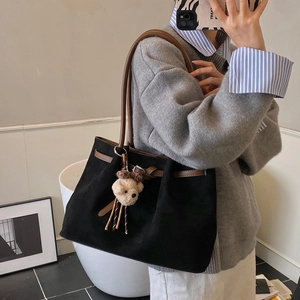 Detail of black suede tote bag featuring brown leather trim and cute plush bear charm
