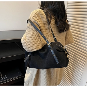 Detail of black suede shoulder bag with adjustable strap and golden metal eyelets