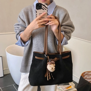 Detail of black suede tote bag with brown leather handles and plush bear charm decoration
