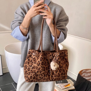 Detail of leopard print tote bag with brown leather handles and plush bear charm