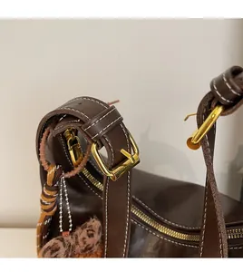 Close-up of brown leather bag showing white stitching, gold hardware and leopard charm