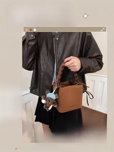 Close-up of caramel leather bucket bag featuring chain handle and cute bear charm