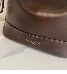 Close-up of brown leather bag with white contrast stitching and gold logo details
