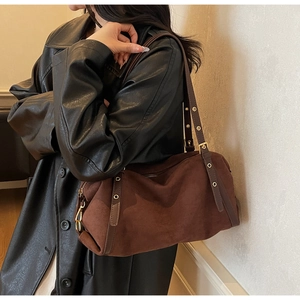 Detailed view of dark brown suede shoulder bag with gold metal buckle and leather strap