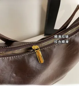 Detail of smooth gold zipper and white stitching on brown leather bucket tote bag