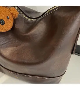 Detail of dark brown leather tote showing soft texture, contrast stitching and bear charm