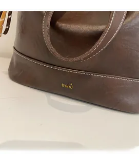 Detailed close-up of dark brown leather tote bag with white contrast stitching and gold logo