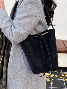 Chic black leather bucket bag for winter with long drawstring straps on a model in grey coat