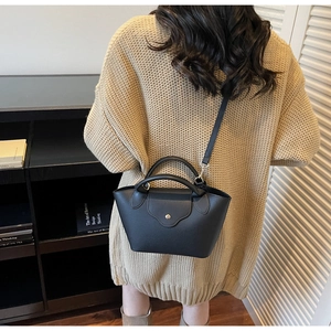 Close-up of a black lychee-textured leather crossbody bag on a beige knit sweater
