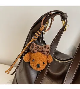 Brown plush puppy charm with leopard bow and woven strap on leather shoulder bag
