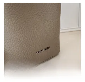 Gros plan sur le grain de cuir litchi et le logo sur le sac seau couleur taupe