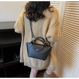 Detail of black lychee grain leather mini handbag featuring a golden round metal buckle