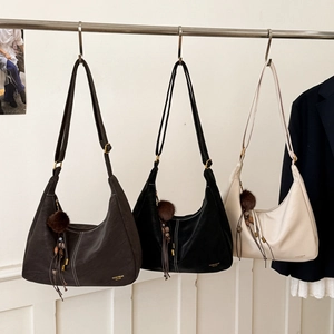 Detail view of half-moon shoulder bags in brown, black, and beige with fuzzy pendants