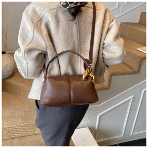 Détail d'un sac à bandoulière en cuir grainé marron foncé avec boucle dorée sur modèle