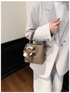 Detail of lychee pattern leather bucket bag with chain handle and plush bear charm
