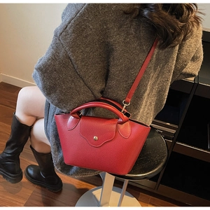 Detail view of red lychee textured handbag showing the top handle and gold snap button