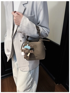 Detail of coffee brown bucket bag with lychee grain texture and cute plush bear charm