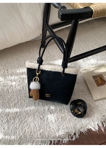 Detail of crossbody bag with faux shearling trim and brown glove charm on a white rug